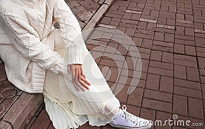 White oversized sweater, light skirt and white sneakers. Details of street-style clothing. Stock Photo