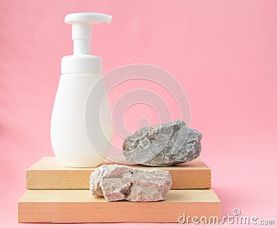 White packaging with a dispenser stands on a wooden stand and natural stones on a pink pastel background. Spa care concept, layout Stock Photo