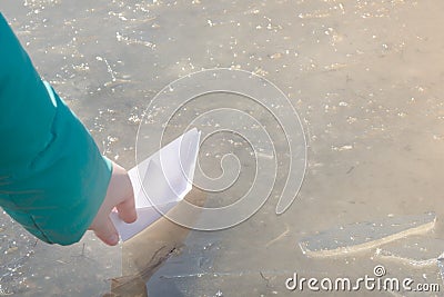 White paper ship is sent on journey into first spring puddle. Child`s hand with origami in sunlight. Early spring mood concept, Stock Photo