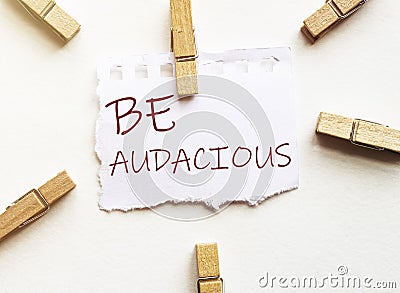 White paper with text Be Audacious with clothespins on white background Stock Photo
