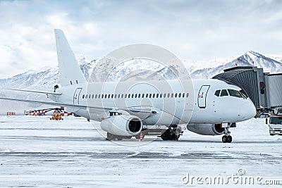 White passenger airliner at the jetway at winter airport apron on the background of high scenic mountains Stock Photo