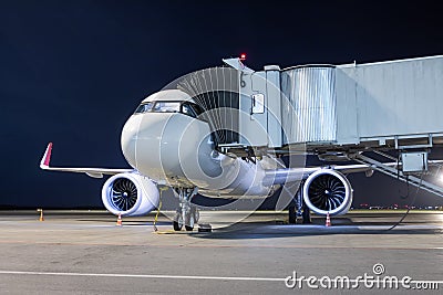 A white passenger jet plane at the air bridge connected to an external power supply on an airport night apron Stock Photo