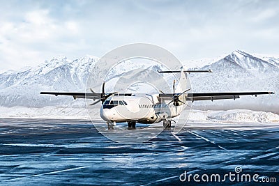 White passenger turboprop aircraft on the winter airport apron on the background of high scenic mountains Stock Photo