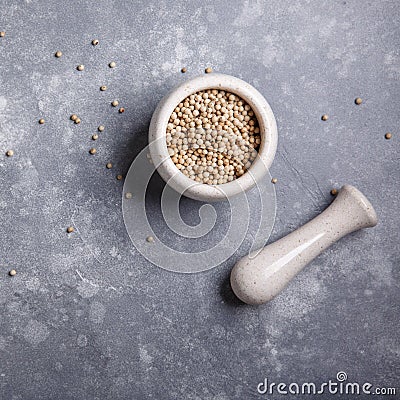 White peppercorns in a mortar for spices. Stone mortar and pestle full white pepper on gray background. Top view. Copy space Stock Photo