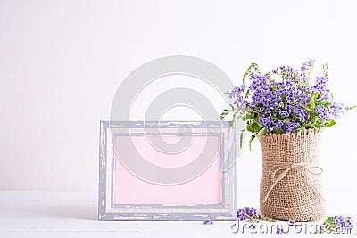 White picture frame with lovely purple flower in vase on white wooden table Stock Photo