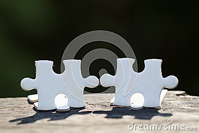 2 white pieces of puzzle stand on wooden table isolated on black background, concept of connecting Stock Photo
