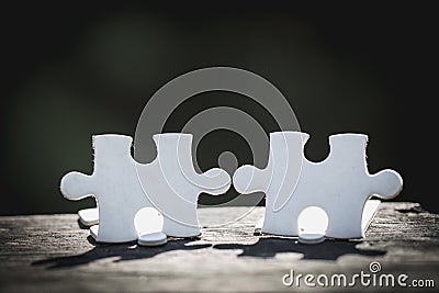 2 white pieces of puzzle stand on wooden table isolated on black background, concept of connecting Stock Photo