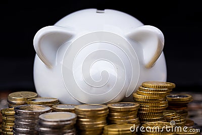White piggy bank behind coins in dark setting Stock Photo