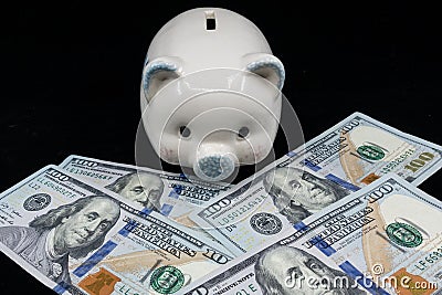 White piggy bank isolated close-up on a pile of United States currency against a black background. Wealth and savings concept. Stock Photo