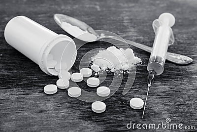 White pill, syringe and heroin on spoon on the old wooden background. Drug addiction. Black and white shot Stock Photo