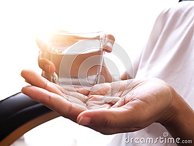 White pill tablet on hand and glass of water to take medicine to cure illness Stock Photo