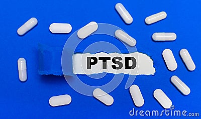 White pills lie on a beautiful blue background. In the center is white paper with the inscription PTSD. Medical concept. View from Stock Photo