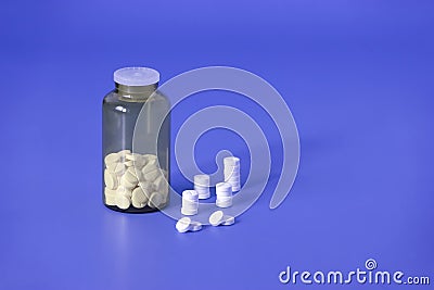 White pills, medical tablets, placebo or vitamins and brown transparent bottle with medicine on dark blue background Stock Photo