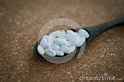 White pills and medicines in the wooden spoon on a brown cork background. Stock Photo