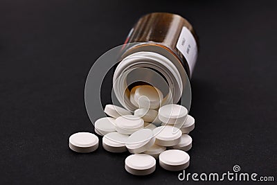 White pills spilled from fallen pill bottle. Pills and medicine container lying on black background illustrating drug addiction. C Stock Photo