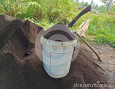 white plastic barrel containing ground manure. around it is a pile of fertilizer and two hoes Stock Photo