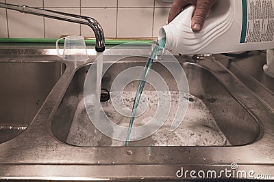 From white plastic bottle a blue liquid is poured into a wash basin Stock Photo