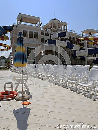 white plastic deck chairs standing in front of each other near the swimming pool with blue tile Editorial Stock Photo