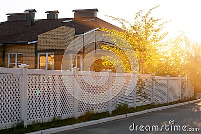 White plastic fence around a typical house in a cottage village. Concept of landscaping, protection, fencing of a territory Stock Photo