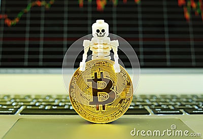 A skeleton and a gold bitcoin standing on a notepad of a notebook computer with a stock graph in the background Editorial Stock Photo