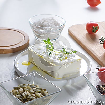 In a white plate cheese with greens, peeled sunflower seeds and tomatoes on an unused kitchen table Stock Photo