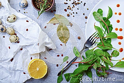 Top view of a table with bay leaves, green salad leaves, quail eggs, a half of lemon on a light gray background. Stock Photo