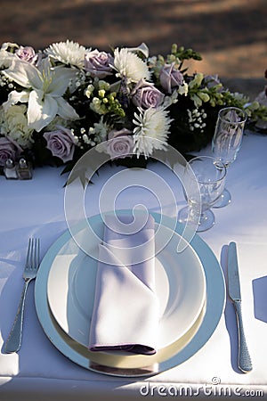 White plate with light violet napkin, clearwine glass and florals - lilis, roses and chrysanthemum. Wedding reception table Stock Photo