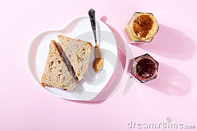 White plate in shape of heart with sandwiches with peanut butter and strawberry jelly on pink background. Top view Stock Photo