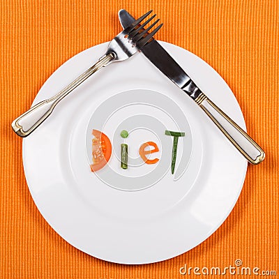 White plate with word diet made of pieces of vegetables on orange tablecloth background. Fork and knife lying on it. Stock Photo