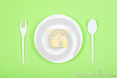 White plate with yellow gift box, spoon, fork on green background. Festive, birthday, Gift pastel minimal background Stock Photo