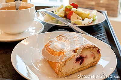 On white plates: cherry strudel, greek salad and a cup of tea on brown salver. Stock Photo