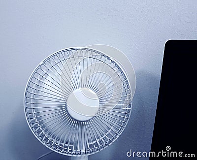 A white portable fan in working mode stands next to a laptop Stock Photo