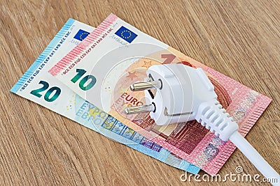 White power plug over euro banknotes on a brown wooden surface. Expensive energy and cost of electricity concepts Stock Photo