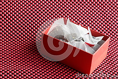 White pyramid tea bags with black and green tea flavored with fruits and berries lie in a red souvenir gift box on a textured red Stock Photo