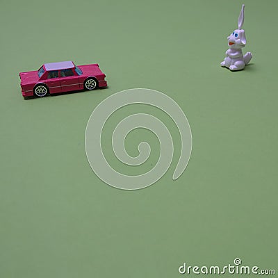 A white rabbit is waiting for a pink car coming towards him on a green background with copy space. Minimal composition for Chinese Stock Photo