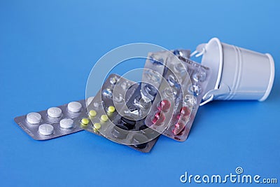 White, red, black and yellow tablets in the plates are in a decorative bucket, white and blue background. Medicine, health concept Stock Photo