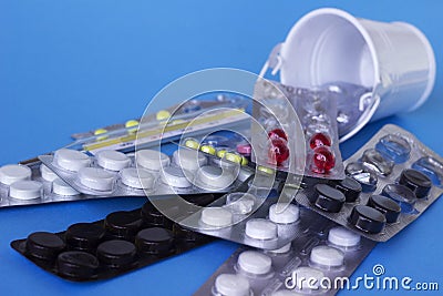 White, red, black and yellow tablets in the plates are in a decorative bucket, white and blue background. Medicine, health concept Stock Photo