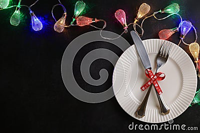 White plate with knife and fork tied with red festive ribbon. Garland of colorful lights. Place for text Stock Photo