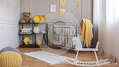 White rocking horse in elegant grey and yellow baby room with industrial shelf and wooden cradle Stock Photo