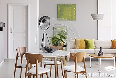 White round table with wooden chairs in the middle of stylish living room with industrial lamp, comfortable couch and golden lime Stock Photo