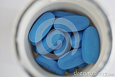 White rounded dose with heap of blue oval pills as a symbol of medicine, healing and pharmacy Stock Photo