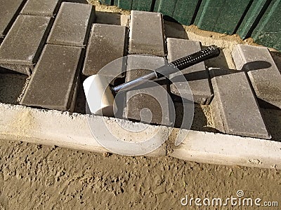 White rubber mallet close up and unfinished work on laying gray paving slabs `Brick` Stock Photo