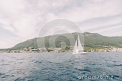 White sailboat sails on the sea along the mountainous coast Stock Photo