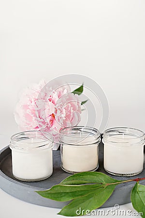 white scented candles on a cement tray and peony flower. soy wax aroma candles in glass unbranded package. home Stock Photo