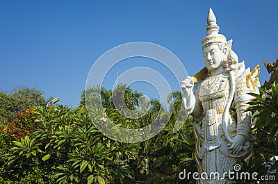 White sculpture of Spirit Nat guard surrounded by tropical trees at Kyauktawgyi Pagoda complex in Mandalay Stock Photo