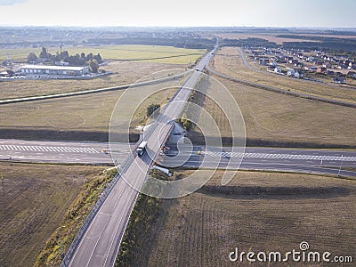 White Semi Truck with Cargo Trailer Passing Highway Overpass. 18 Wheeler car on road, drive towards Loading Warehouses. Aerial Stock Photo