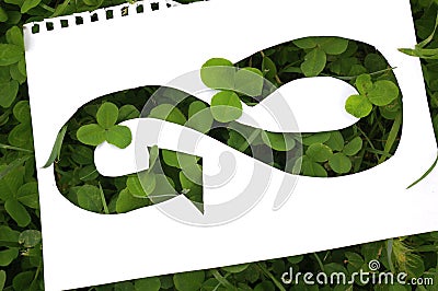 White sheet of notepad with the infinity symbol cut into the paper. Circular economy symbol on green clover background. Stock Photo