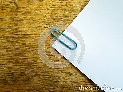 White sheet of paper on a wooden table with a blue paper clip Stock Photo