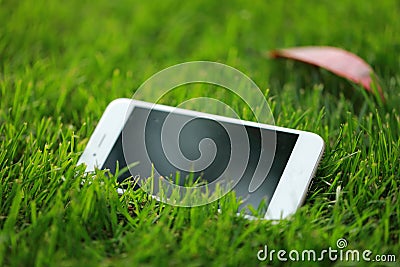 A white smart phone cellphone on green grass lawn in summer spring park garden at sunny day Stock Photo