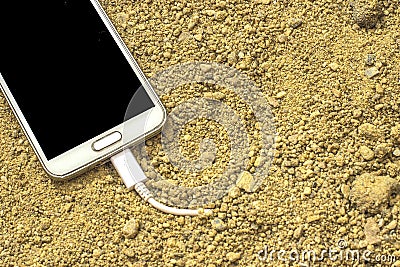 White smartphone with a charger plugged into the sand. front and back background blurred Stock Photo